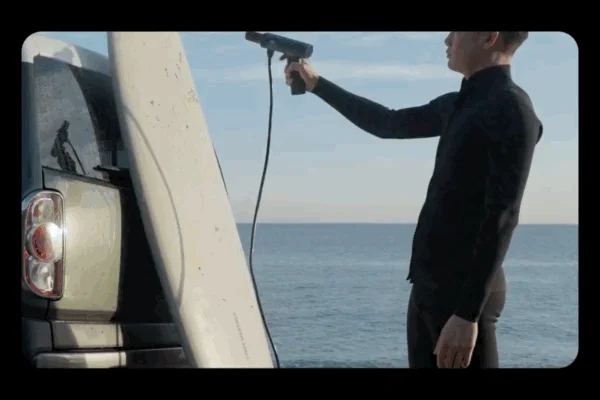 海辺で車に立てかけたサーフボードを携帯式の洗浄機で洗っている様子