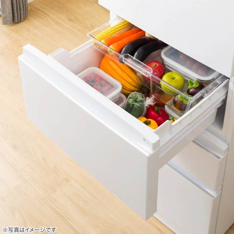 白い冷蔵庫の野菜室が引き出され、トレイに整理されたトウモロコシ、ナス、カボチャ、リンゴなどの色とりどりの新鮮な野菜や果物がきれいに収納されている様子