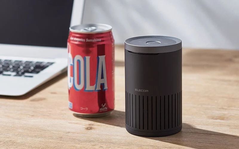 木製のデスクに置かれた赤いコーラの缶と黒い円筒形のデバイス（エレコム製）が写っています。