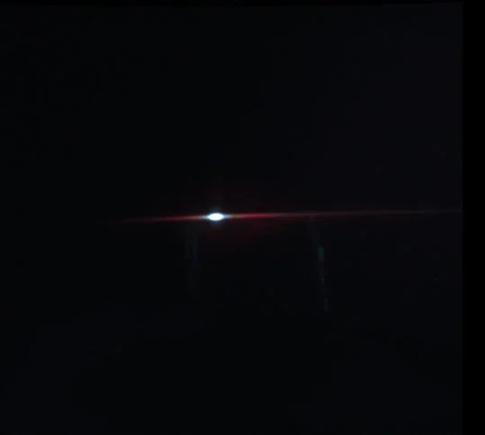 暗い背景の中央に明るい光があり、そこから赤い水平なレンズフレア