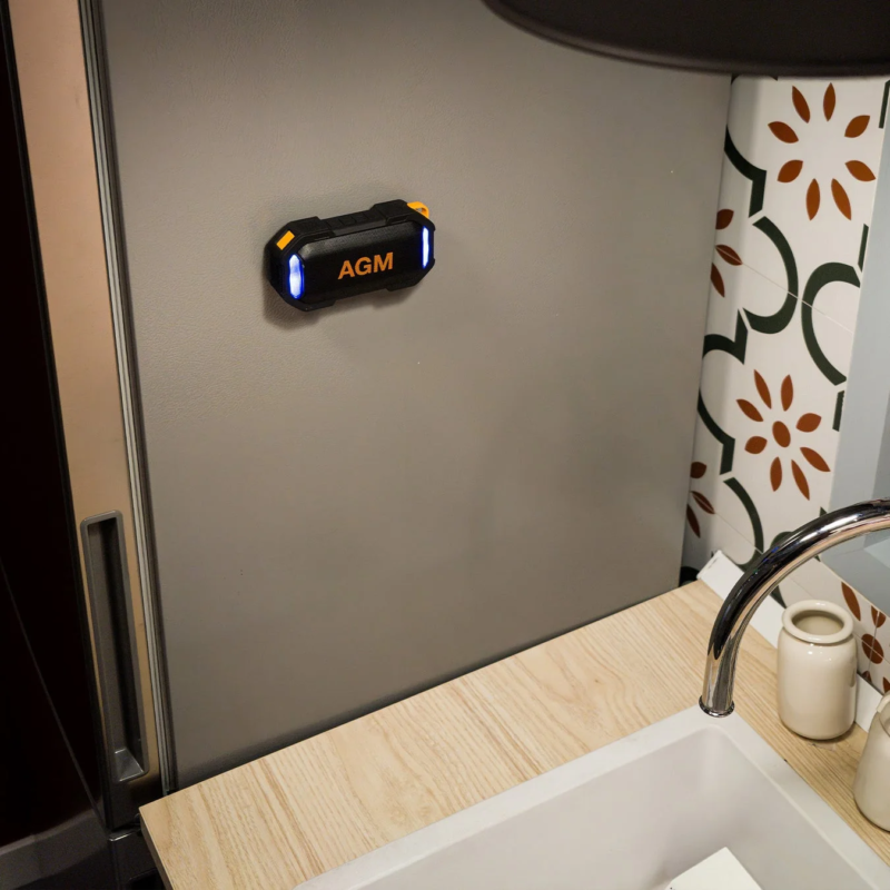 キッチンの冷蔵庫の扉に、青いライトが点灯した黒とオレンジのAGM製ポータブルスピーカーが取り付けられています