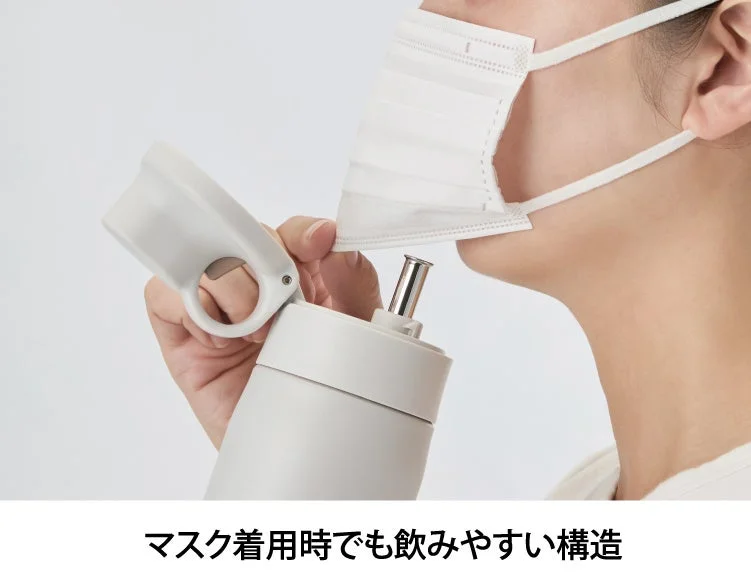 マスクを着用したままでも飲みやすいように設計された水筒を使用している様子です。マスクをずらさずに口元にアクセスできる特殊な構造が特徴です。