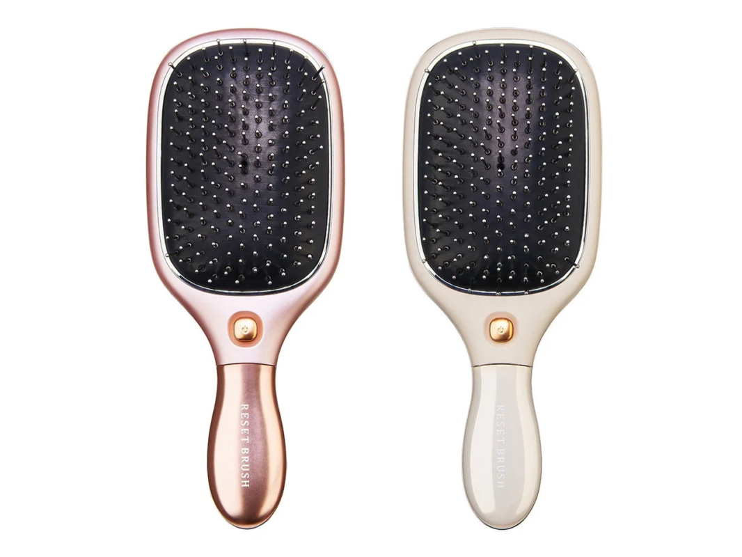 ローズゴールドとベージュの2色の電動ヘアブラシが並べられています。どちらも持ち手には「RESET BRUSH」と書かれており、中央には電源ボタンのようなものが配置されています。