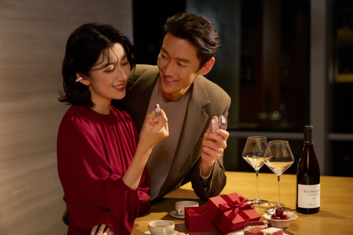 笑顔のカップルがワイヤレスイヤホンを見せ合いながら楽しそうに会話している画像