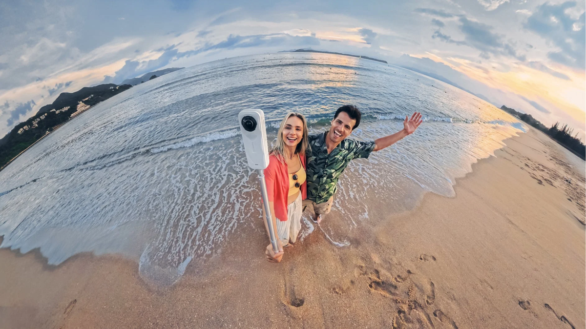 夕焼けのビーチで360度カメラを使うカップル