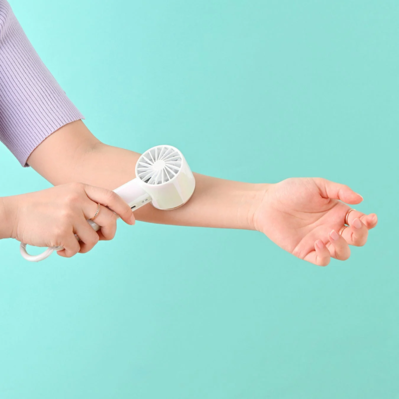 女性が白いハンディファンを腕にあてて冷却している様子