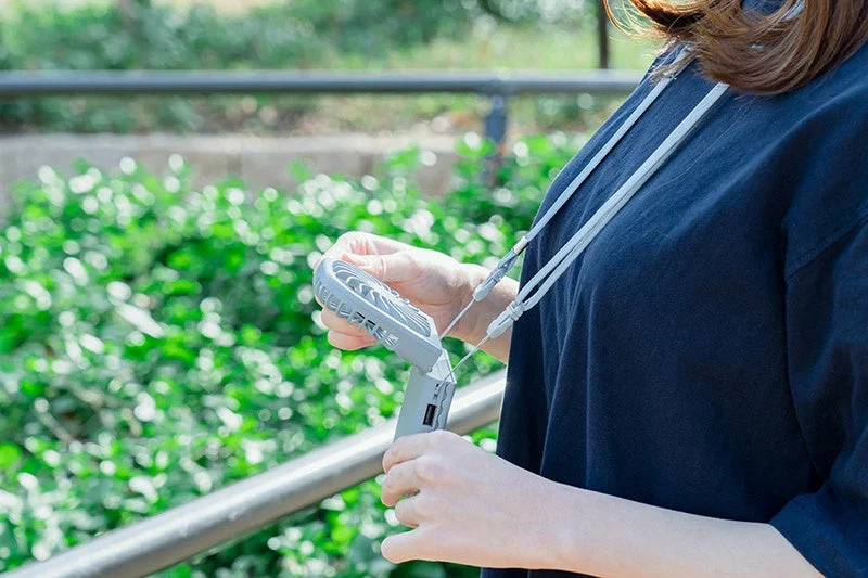 屋外で首から下げたポータブル扇風機を手に持つ人物の様子。