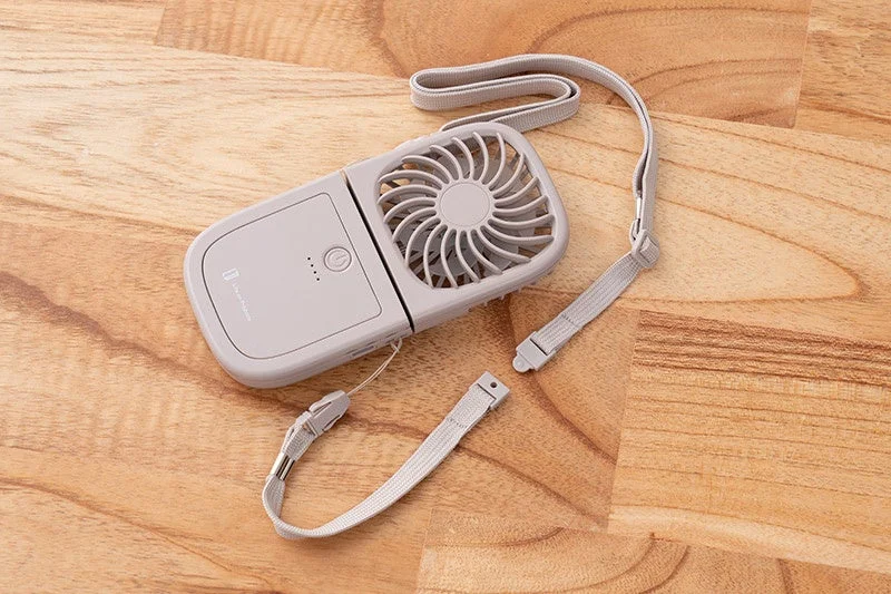 グレーの折りたたみ式携帯扇風機が木製のテーブルに置かれています。