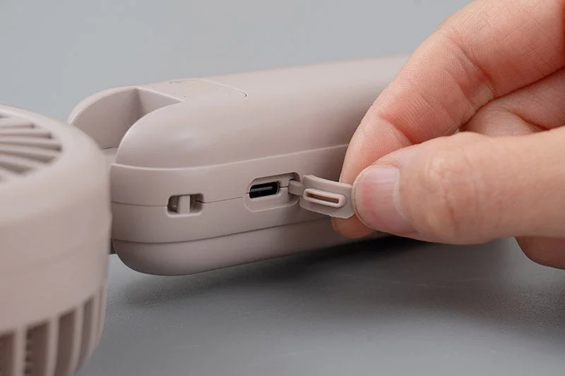 ベージュ色の携帯扇風機のUSB-C充電ポートのカバーを、指で開いている様子