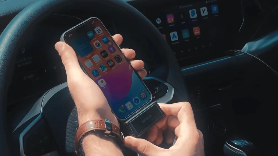 車内でハンドル近くにiPhoneとBelkin製のデバイスを持つ手のクローズアップ