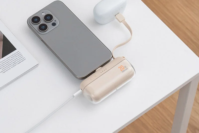 白いテーブルの上で、スマートフォンとワイヤレスイヤホンケースがモバイルバッテリーに接続され、同時に充電されている様子