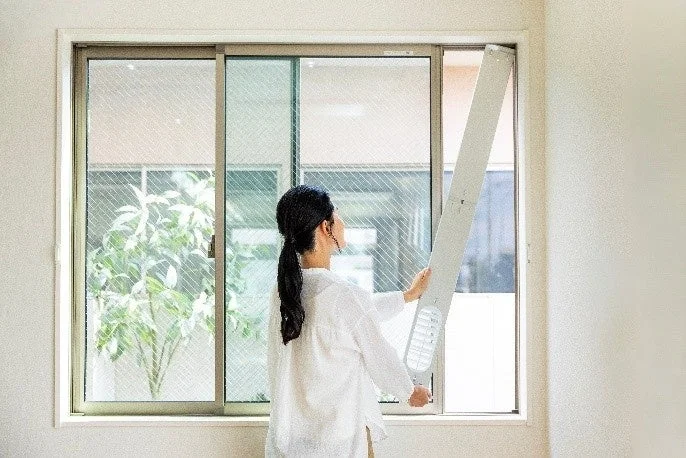 窓に細長い白い器具を取り付けている女性