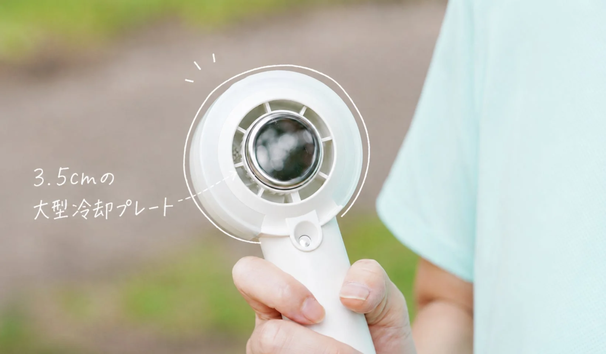 屋外で白いハンディファンを持っている人物。ファンの中央には「3.5cmの大型冷却プレート」が搭載されており、暑い日に涼しさを提供するポータブル冷却デバイスの機能を示唆しています。