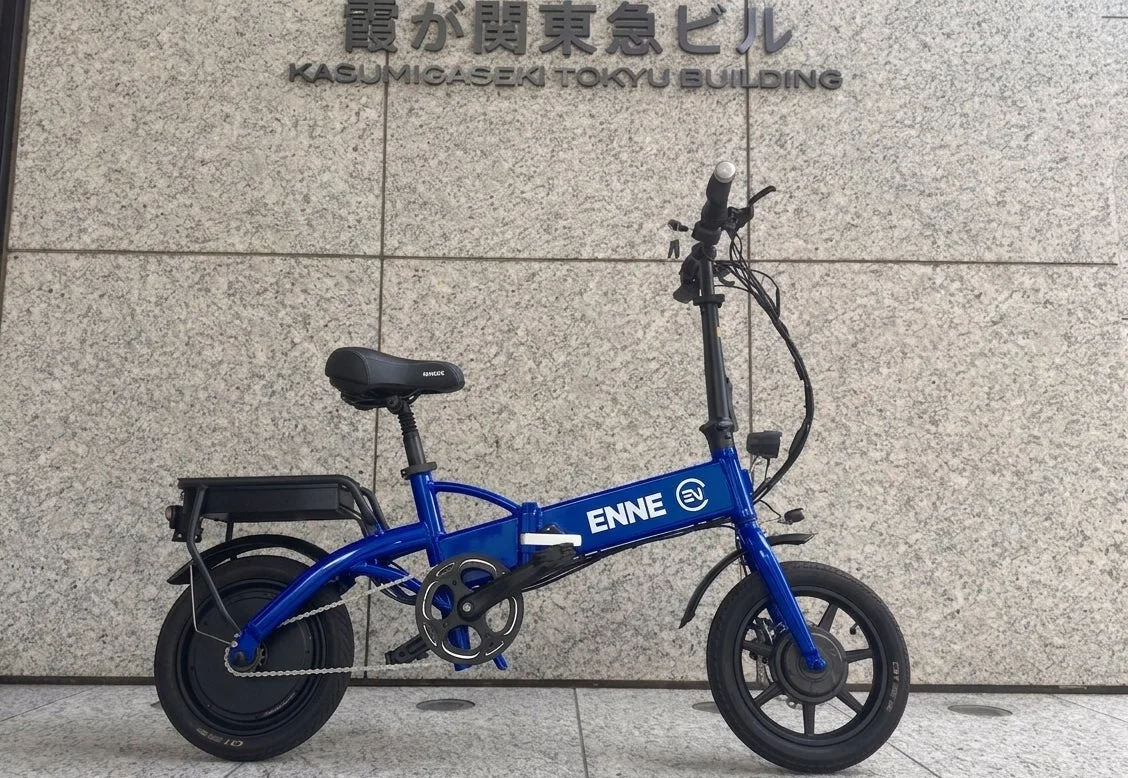 石造りの壁を背景に、青い折りたたみ電動自転車が停められています。壁には「霞が関東急ビル」の文字があり、都会的な景観とEバイクが融合した一枚です。