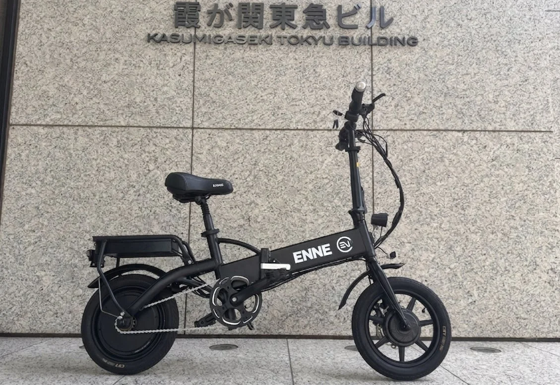霞が関東急ビルの壁を背景に、黒い折りたたみ式電動自転車が停められています。