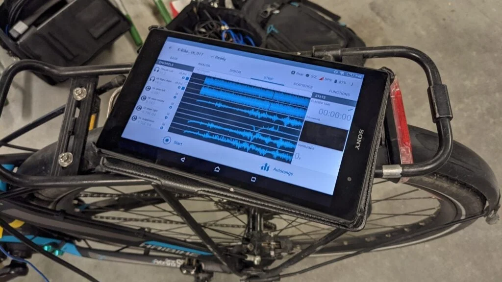 自転車の後部キャリアにSONY製タブレットが固定され、電動自転車のセンサーデータを示す波形グラフが表示されています。走行中のデータ計測や分析用途と考えられます。