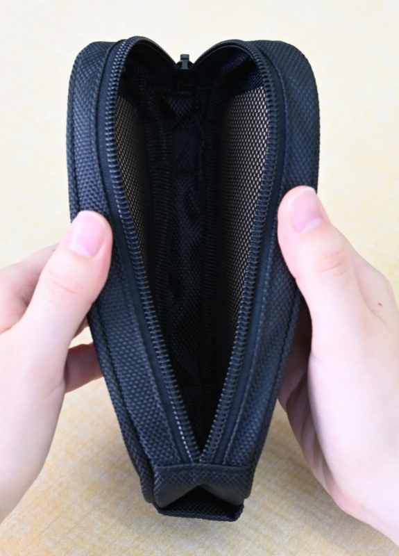 両手で黒いジッパー付きのポーチが開かれている様子。ポーチの内部はメッシュ素材で、小物の収納に適しているように見えます。