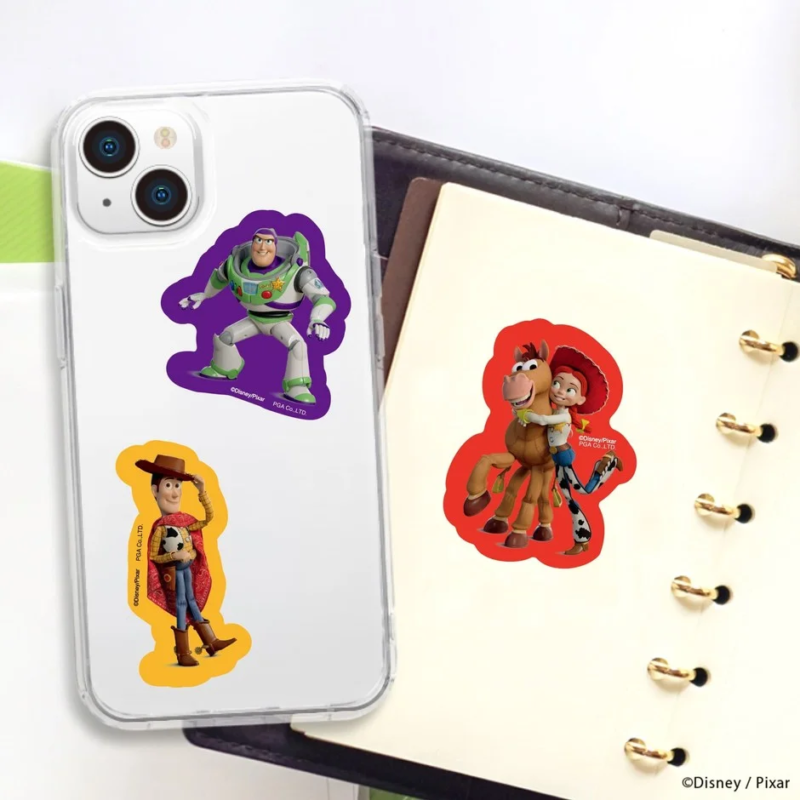 トイストーリーの人気キャラクター、バズライトイヤー、ウッディ、ジェシーとブルズアイのステッカーが貼られたスマートフォンケースとノートの様子。